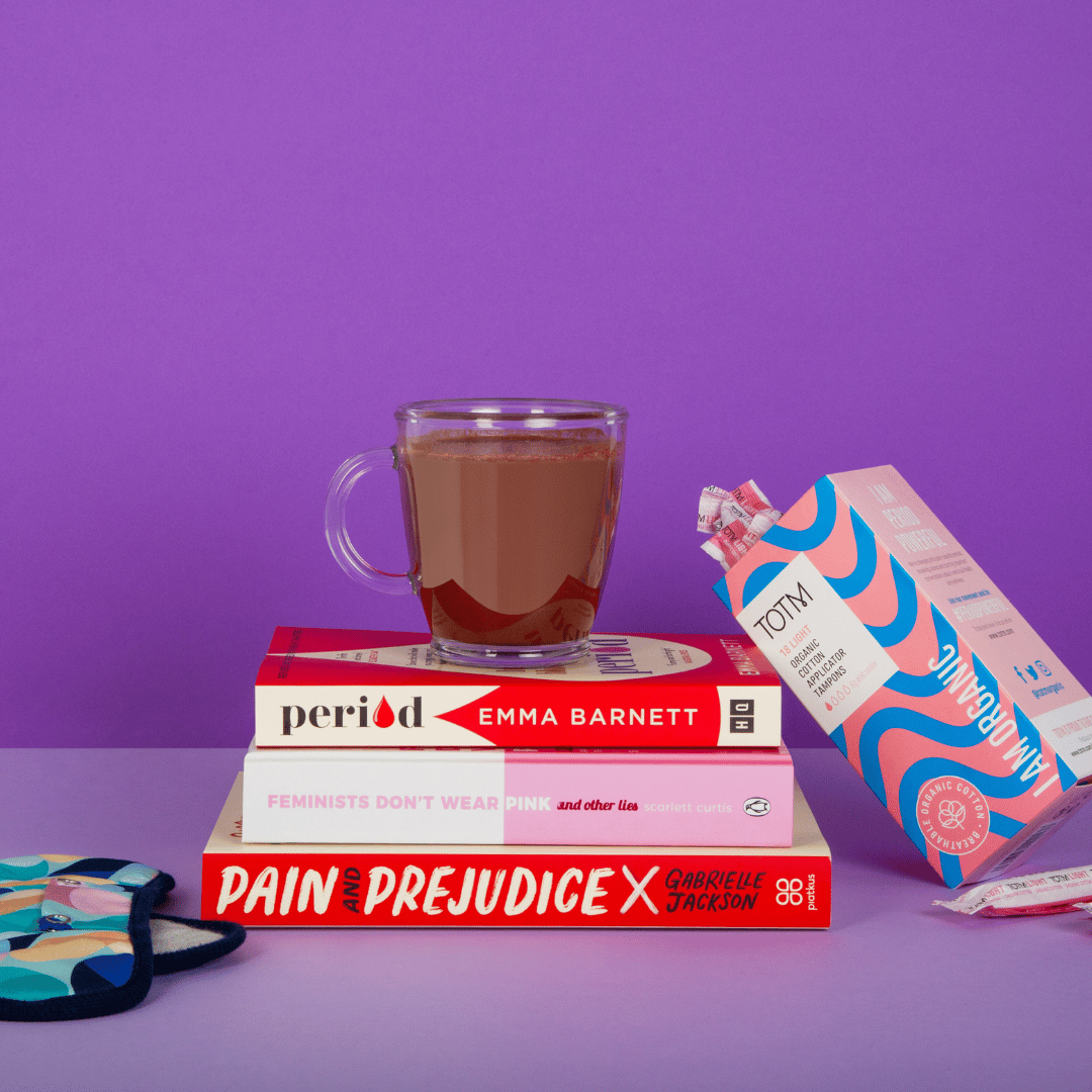 HotTea Mama ashwagandha hot chocolate sat on top of period education books, with tampons and period pants near by on a purple background