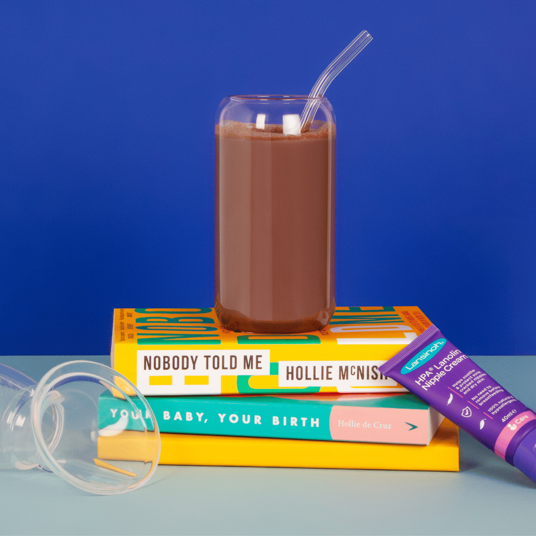 Image of Go With The Flow breastfeeding support Hot Chocolate made as a cold milkshake in a tall jar glass stood on a platform of parenting books