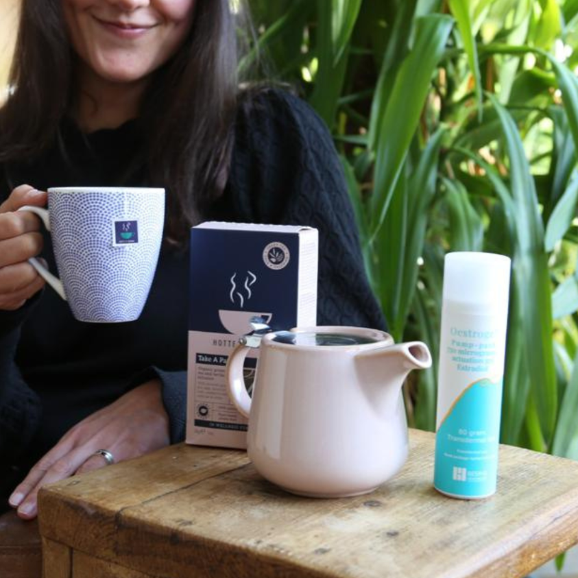 Woman drinking Take a Pause Menopause Tea, with estrogel pack and teapot 